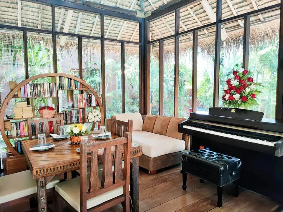 The lounge, with a piano and shelves of books, looking out into the planting