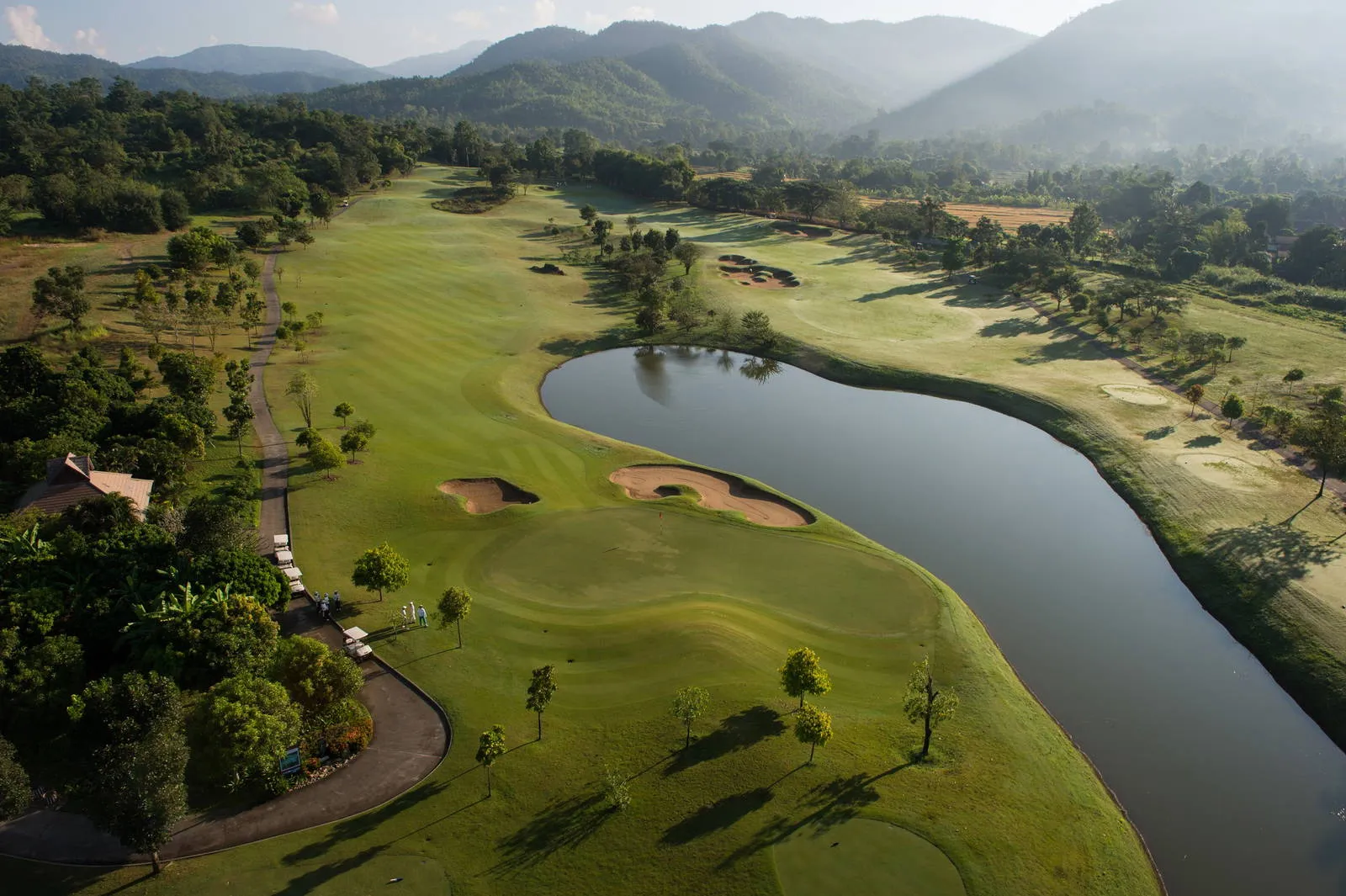 Chiangmai Highlands from the air, fairways curving around a lake with the hills behind
