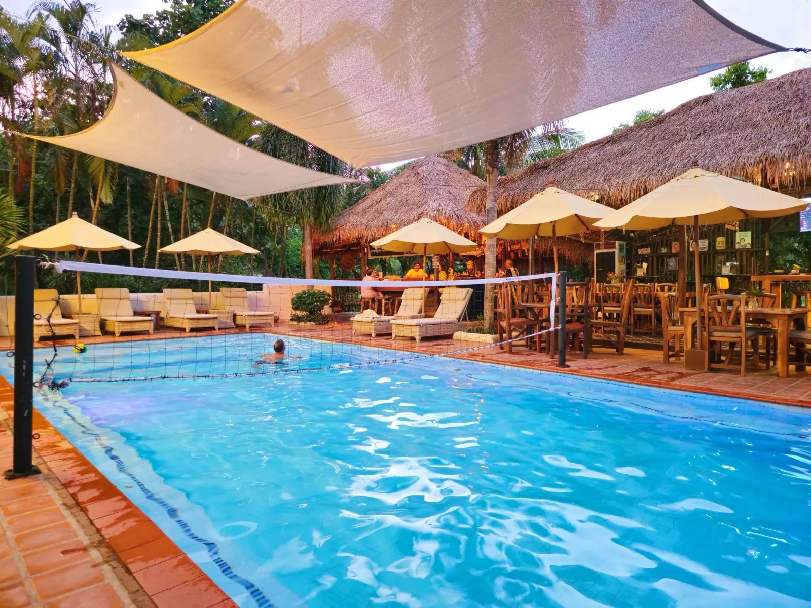 The pool at Baanpong Lodge under its shade sails, the thatched bar and the palms behind it