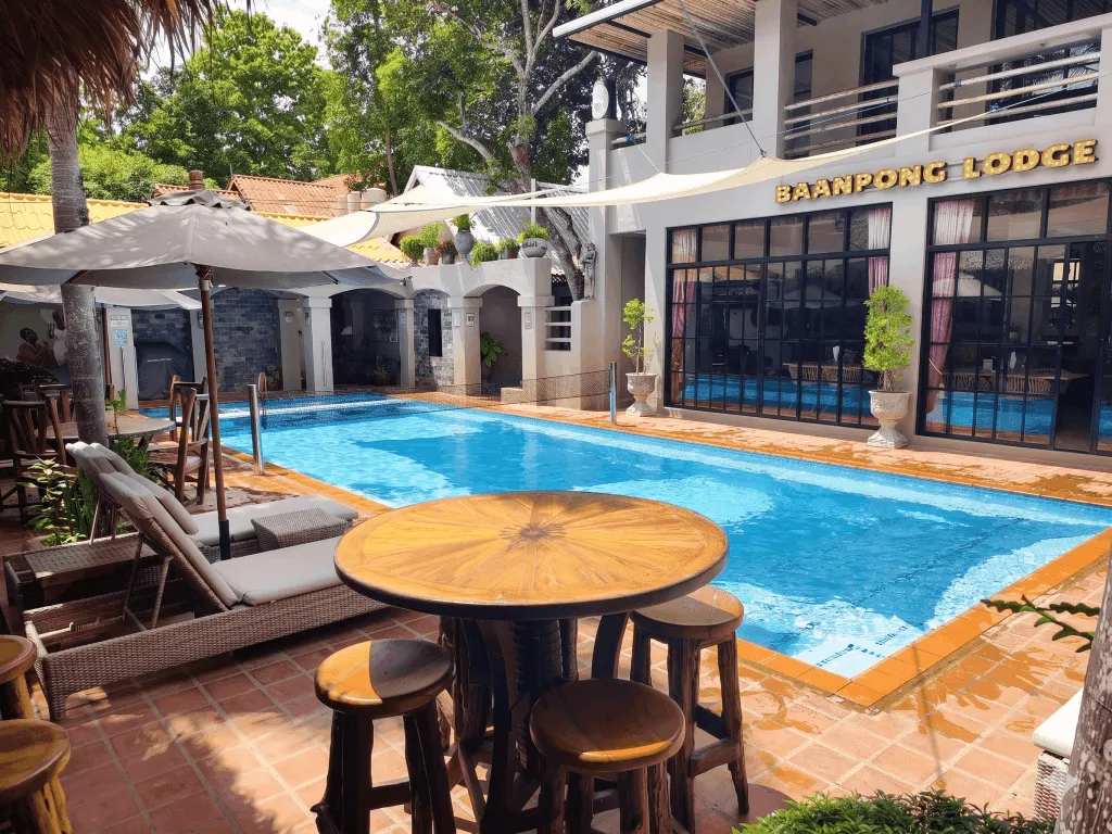 A table and stools at the poolside, with the lodge behind